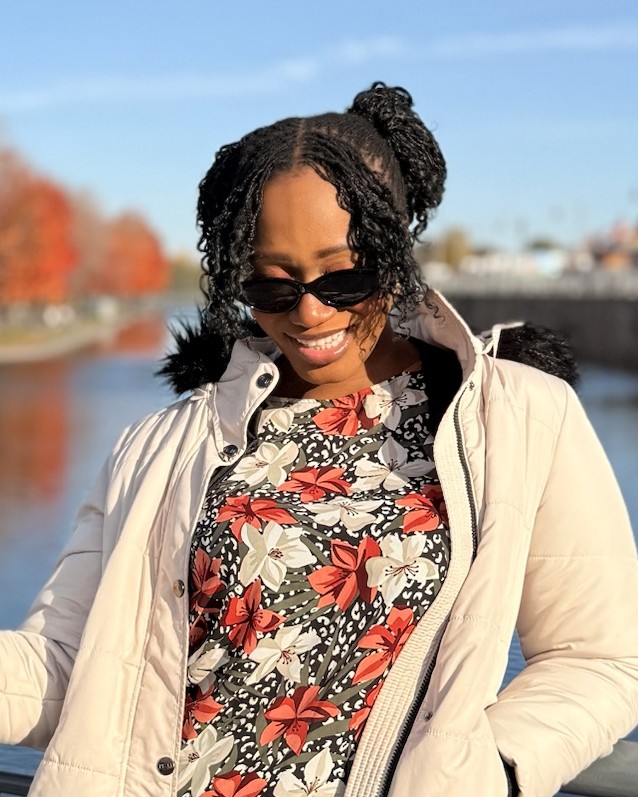 Ruova in a cream jacket by the water