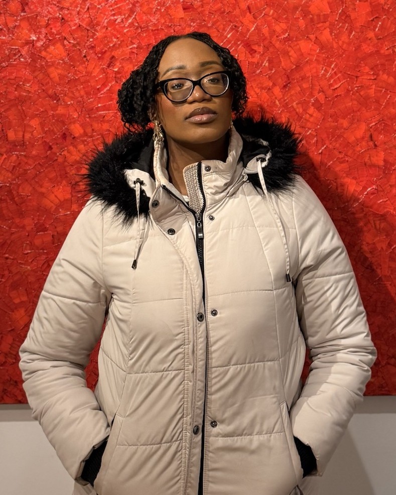 Favour Agbanusi in a winter jacket in front of a red painting